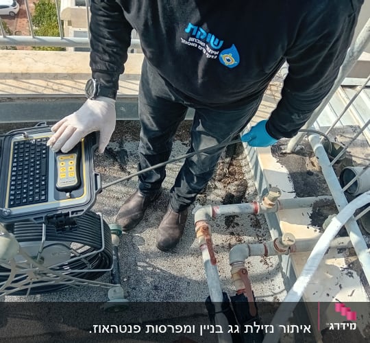 אדם בודק צנרת עם מצלמה ומחשב נייד על גג